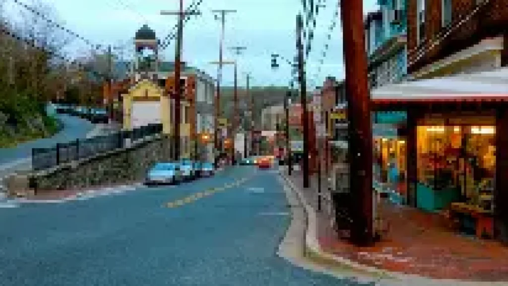 Scenic street view with cars parked along the road, houses, and shops in a small town neighborhood