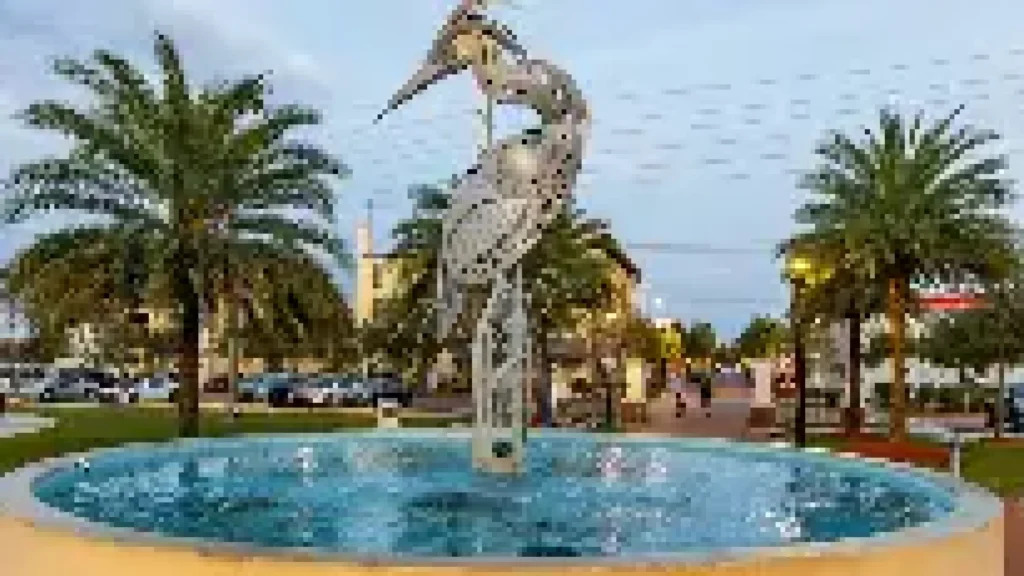 Fountain with a large bird sculpture surrounded by palm trees in a public plaza